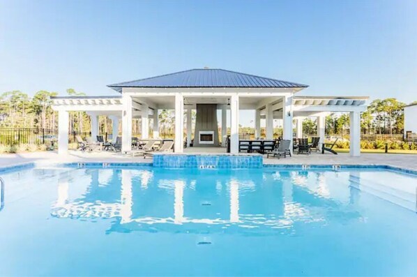 Relax by the pool surrounded by lush greenery and comfortable lounge chairs under a covered pavilion.