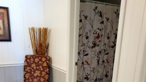 Una habitación con un taburete estampado con motivos florales, una puerta que conduce a otra estancia y un suelo de baldosas.