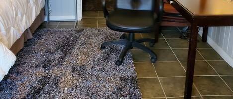 A hotel room with a bed, a desk, a chair, a small table, a lamp, and a rug.