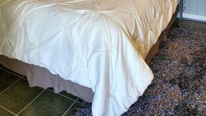 Una cama bien tendida con un cabecero, un cuadro en la pared encima y una lámpara en la mesita de noche.