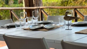 Een eettafel voor buiten, gedekt met helder glaswerk, borden en een decoratief vogelbeeldje.