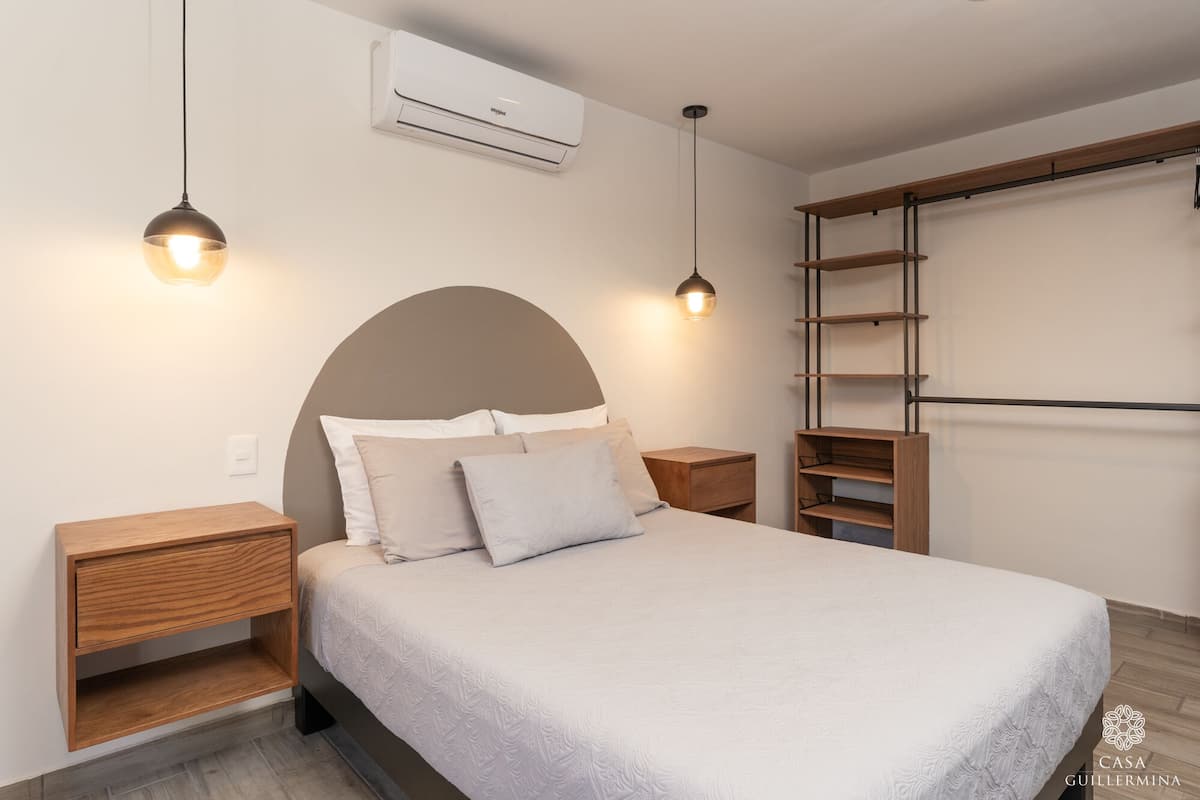 A bedroom with a bed, bedside tables, a wall-mounted air conditioner, and a wooden ladder shelf.