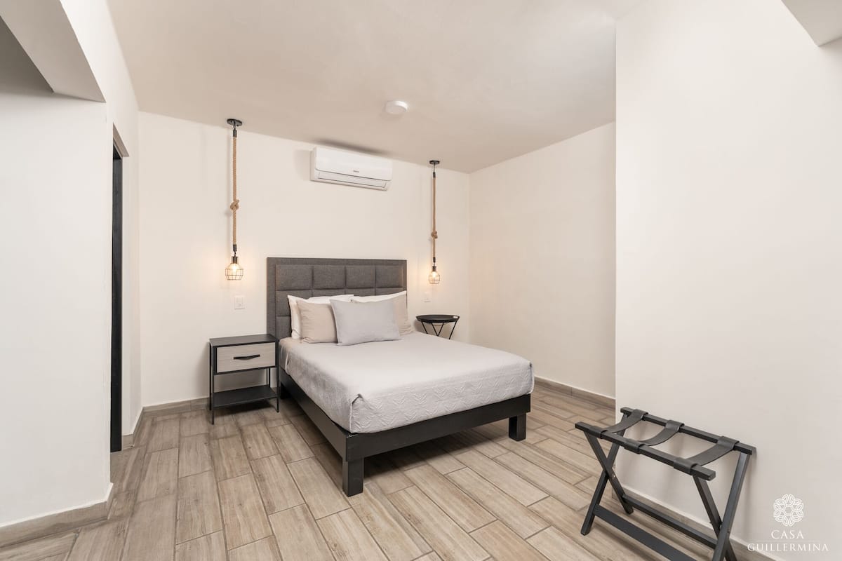A modern bedroom with a bed, bedside tables, an air conditioning unit, and a hanging light fixture.