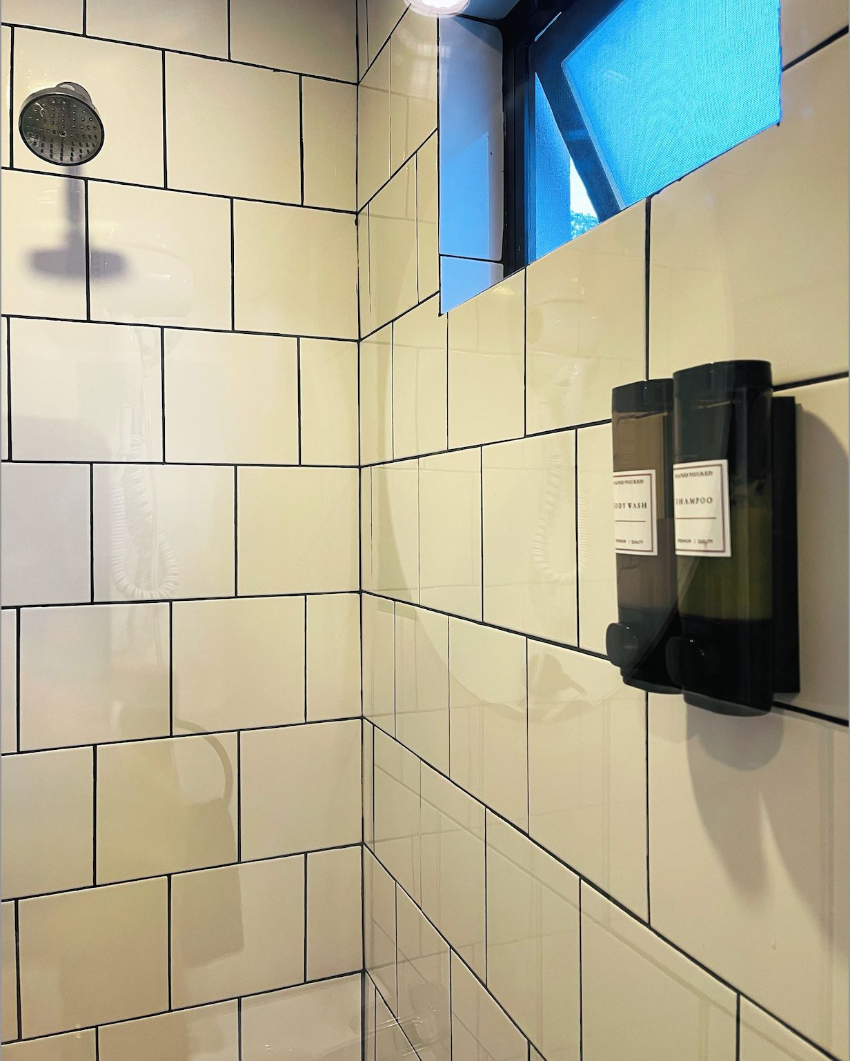 Een badkamer met witte tegels, een douchekop en een zeepdispenser aan de muur.