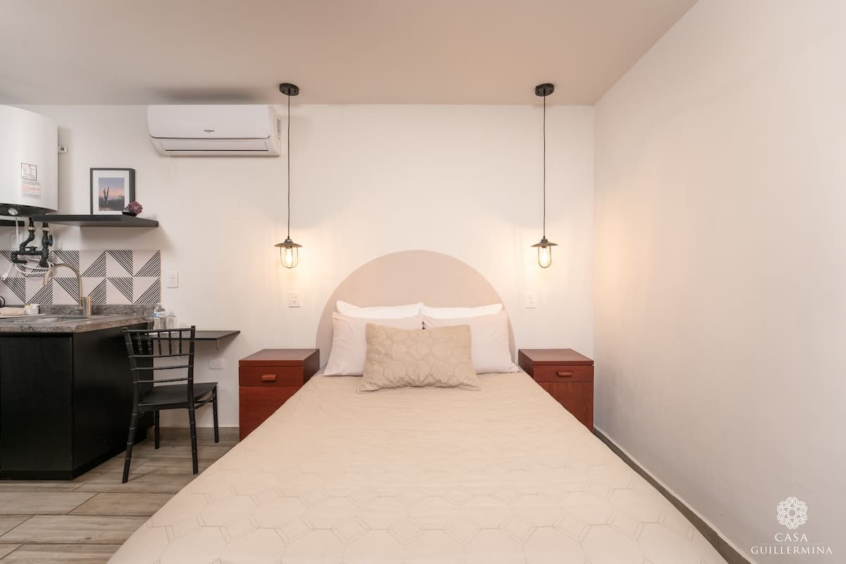 A bedroom with a bed, bedside tables, a desk, and an air conditioning unit.