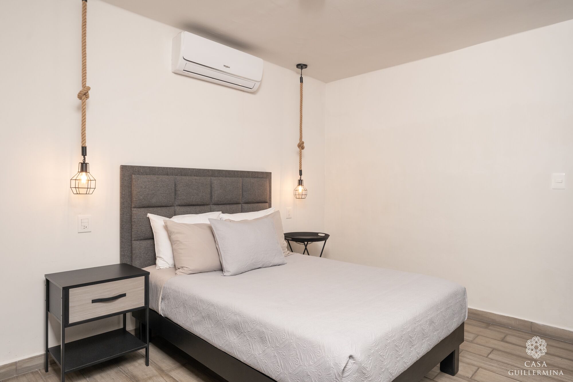 A bedroom with a bed, bedside tables, an air conditioner, and pendant lights.