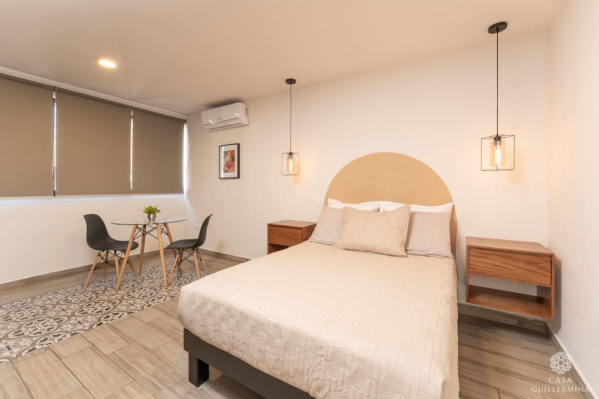 A modern bedroom with a large bed, bedside tables, a desk with chairs, and a window.