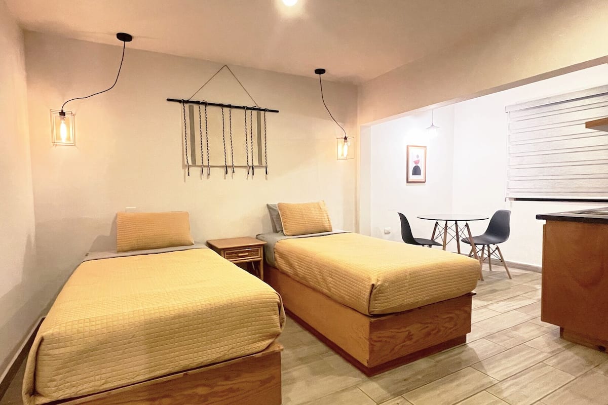 A small, modern room with two single beds, a desk, and a chair.