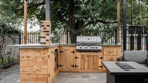 A wooden outdoor kitchen with a grill and a seating area. - Midtown Houston Townhome - Minutes from downtown and night life! (Houston)