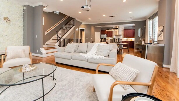 A spacious living area with a sofa, armchairs, and a coffee table. A staircase leads to an upper level. - Midtown Houston Townhome - Minutes from downtown and night life! (Houston)