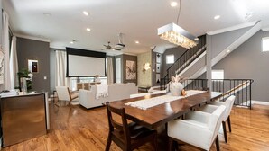 A spacious living room with a wooden dining table and white chairs, a staircase, and a kitchen area. - Midtown Houston Townhome - Minutes from downtown and night life! (Houston)