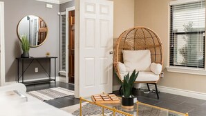 A modern living room with a wicker chair, a round mirror, a console table, and a potted plant. - Midtown Houston Townhome - Minutes from downtown and night life! (Houston)