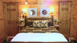Ein Schlafzimmer einer Holzhütte mit einem Bett, zwei Wandleuchten, einem Spiegel und einem gesteppten Kopfteil.