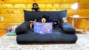 A black sofa with plush toys, a book titled 'Pop-Up Peekaboo,' and a lamp on a wooden floor.