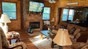 Ein gemütliches Blockhaus-Interieur mit Kamin, Holzmöbeln und einem darüber montierten Fernseher.