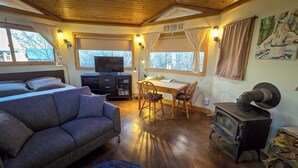 Interior acogedor de una cabaña con sofá, televisión, mesa de comedor y estufa de leña.