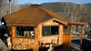 Una cabaña de madera con techo inclinado, ventanas grandes y un porche con sillas.
