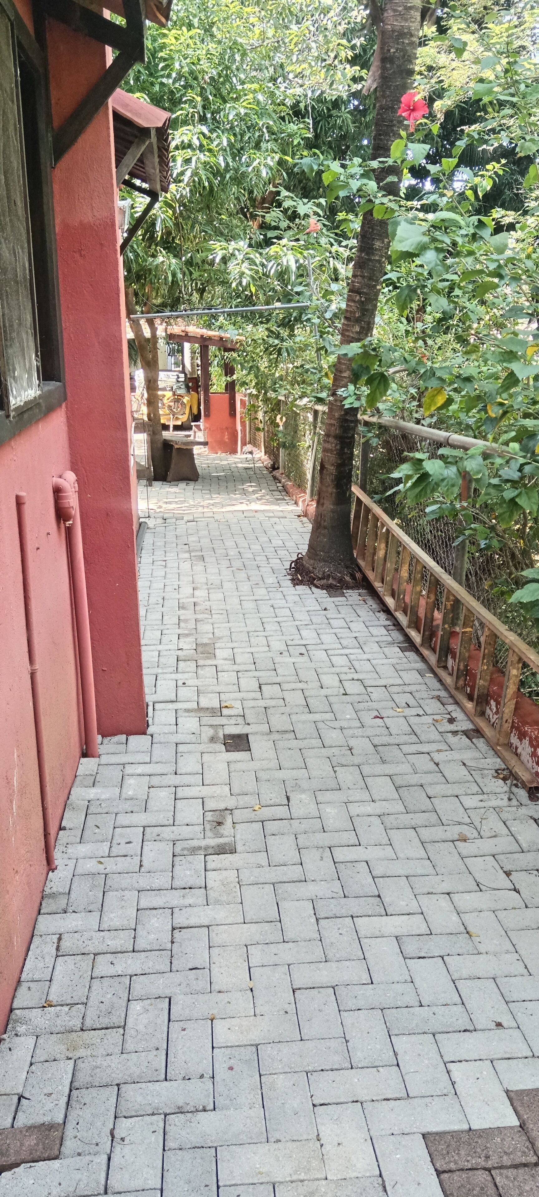 A paved walkway with a brick pattern, bordered by a wooden fence and a red building on one side.