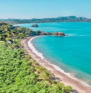 Una zona costera con una playa arenosa curva, aguas turquesas cristalinas y una vegetación exuberante.