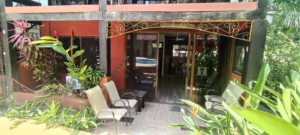 A covered outdoor seating area with chairs and tables, surrounded by potted plants.