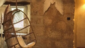 Una habitación con una silla colgante de ratán, una cama con ropa de cama blanca y un adorno de plumas en la pared.