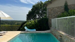 Una piscina con agua azul cristalina, una silla de descanso y un muro de piedra.