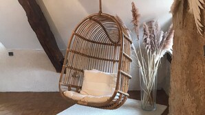 Una habitación con una silla colgante de mimbre, un tapete blanco y plumas de pampa en un jarrón.