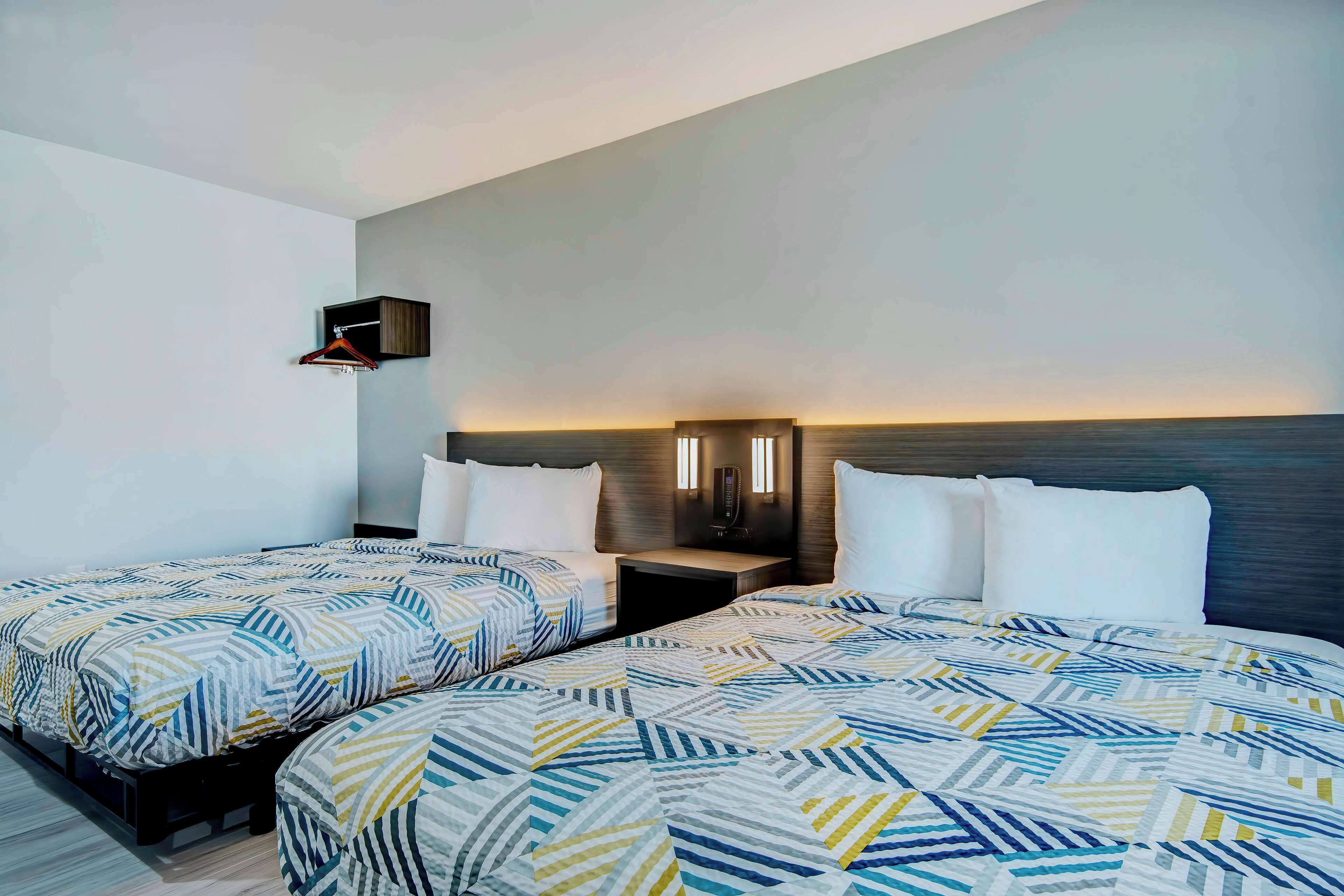 Une chambre d’hôtel avec deux lits, une petite table de chevet, une lampe fixée au mur et un porte-manteau mural.