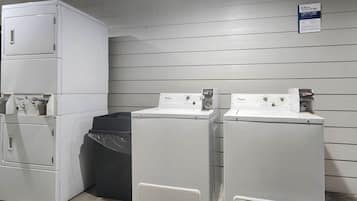 Un área de lavandería con lavadoras y secadoras apiladas, un contenedor de basura y una puerta con un letrero.