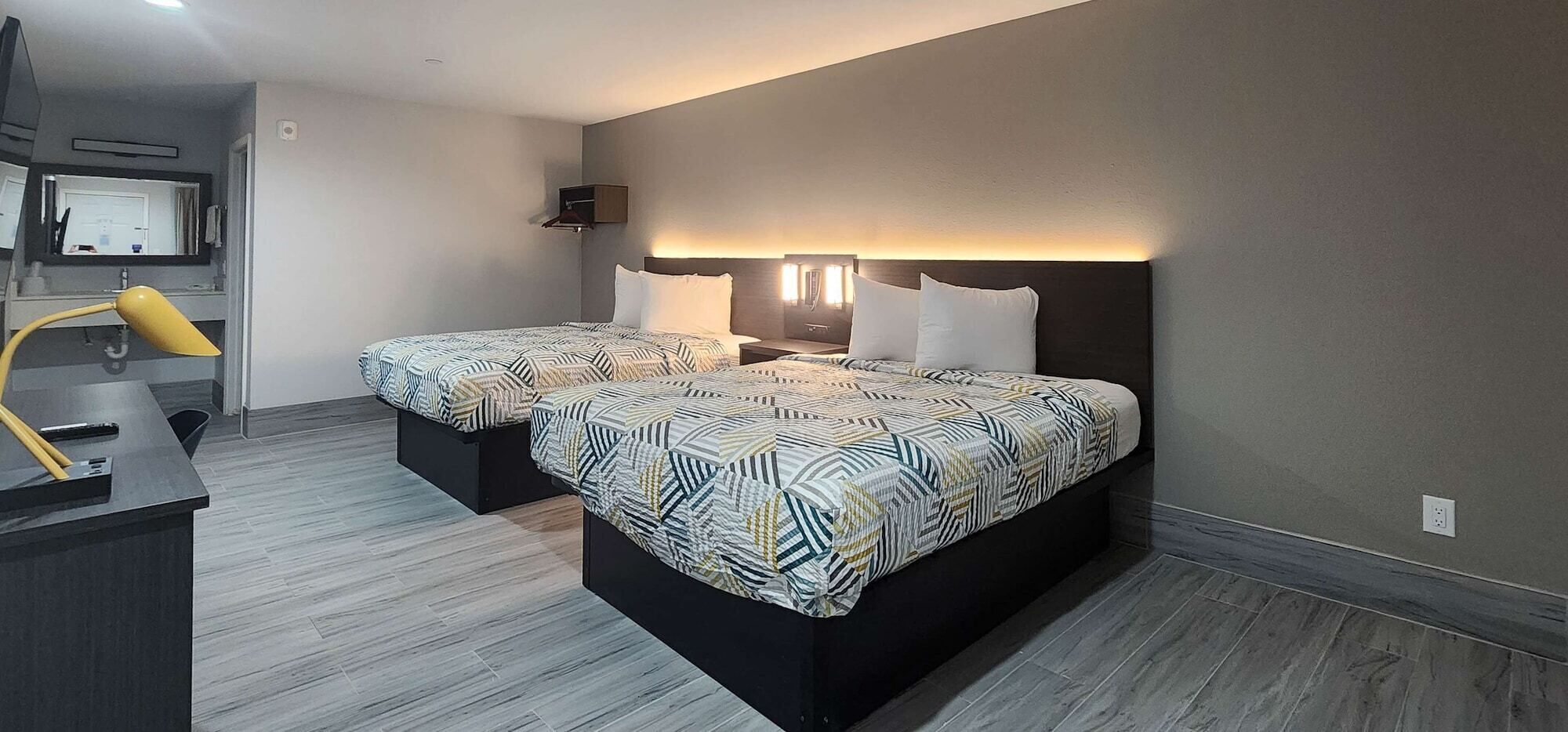 A hotel room with two beds, a desk, and a mirror.