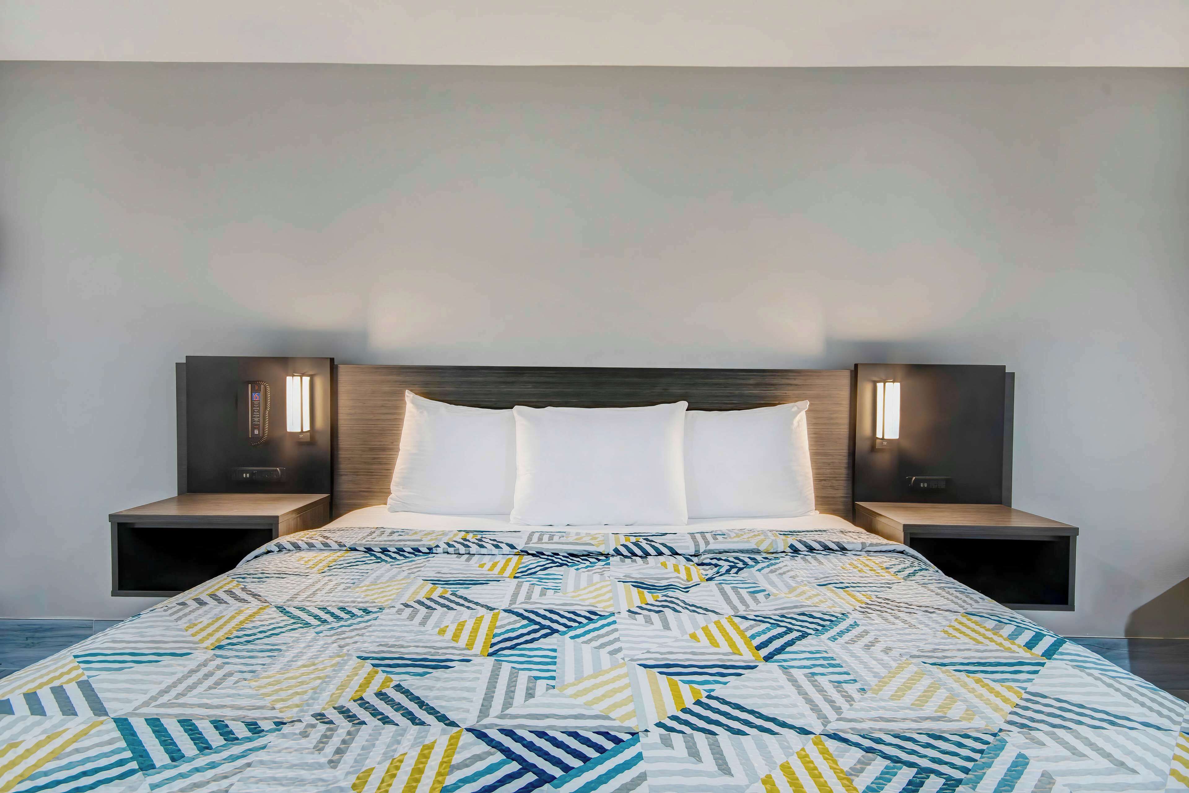 A modern bedroom with a geometric-patterned bedspread, a wooden headboard, and bedside lamps.