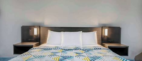A modern bedroom with a geometric-patterned bedspread, a wooden headboard, and bedside lamps.