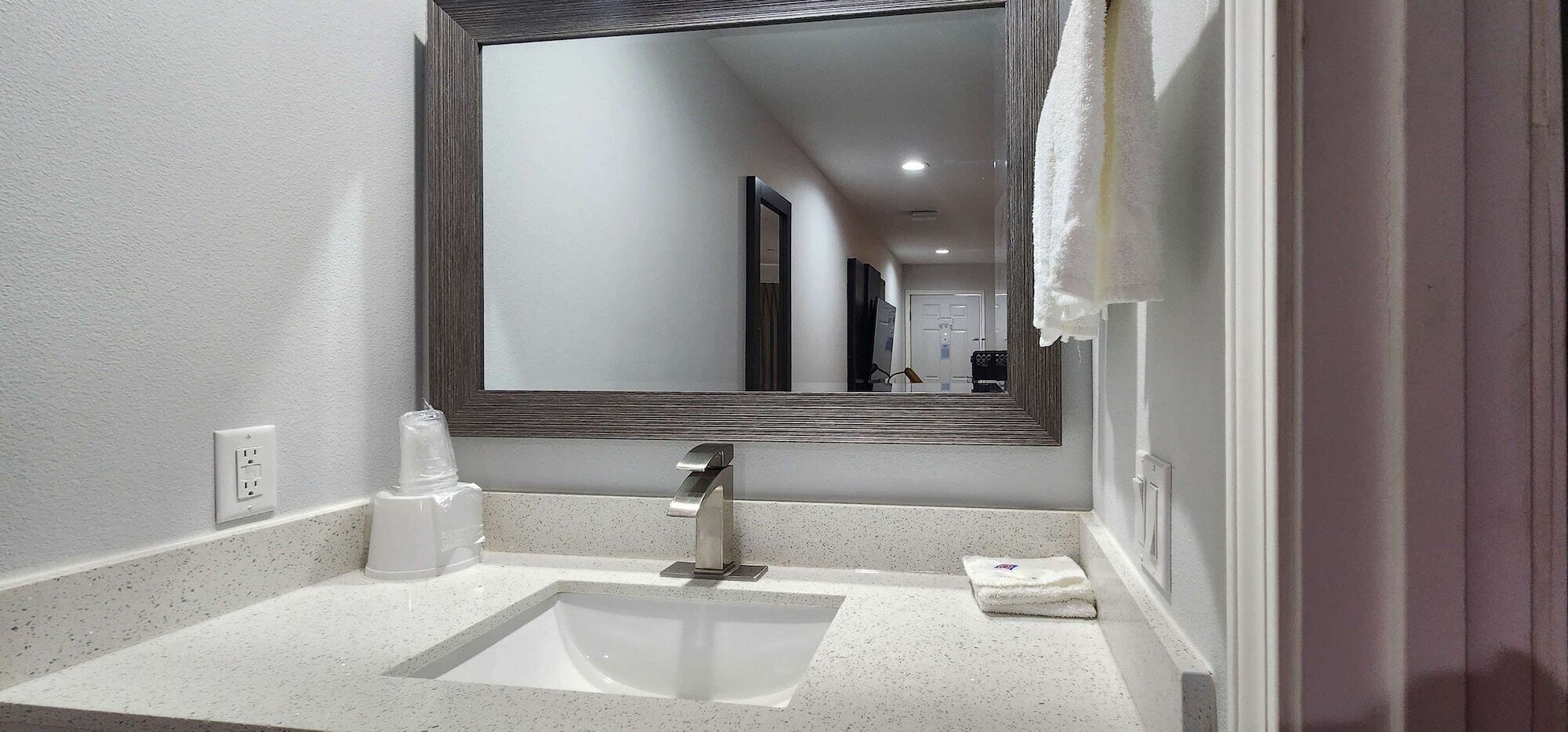 Un baño moderno con un lavamanos blanco, un espejo y una toalla colgada en la pared.