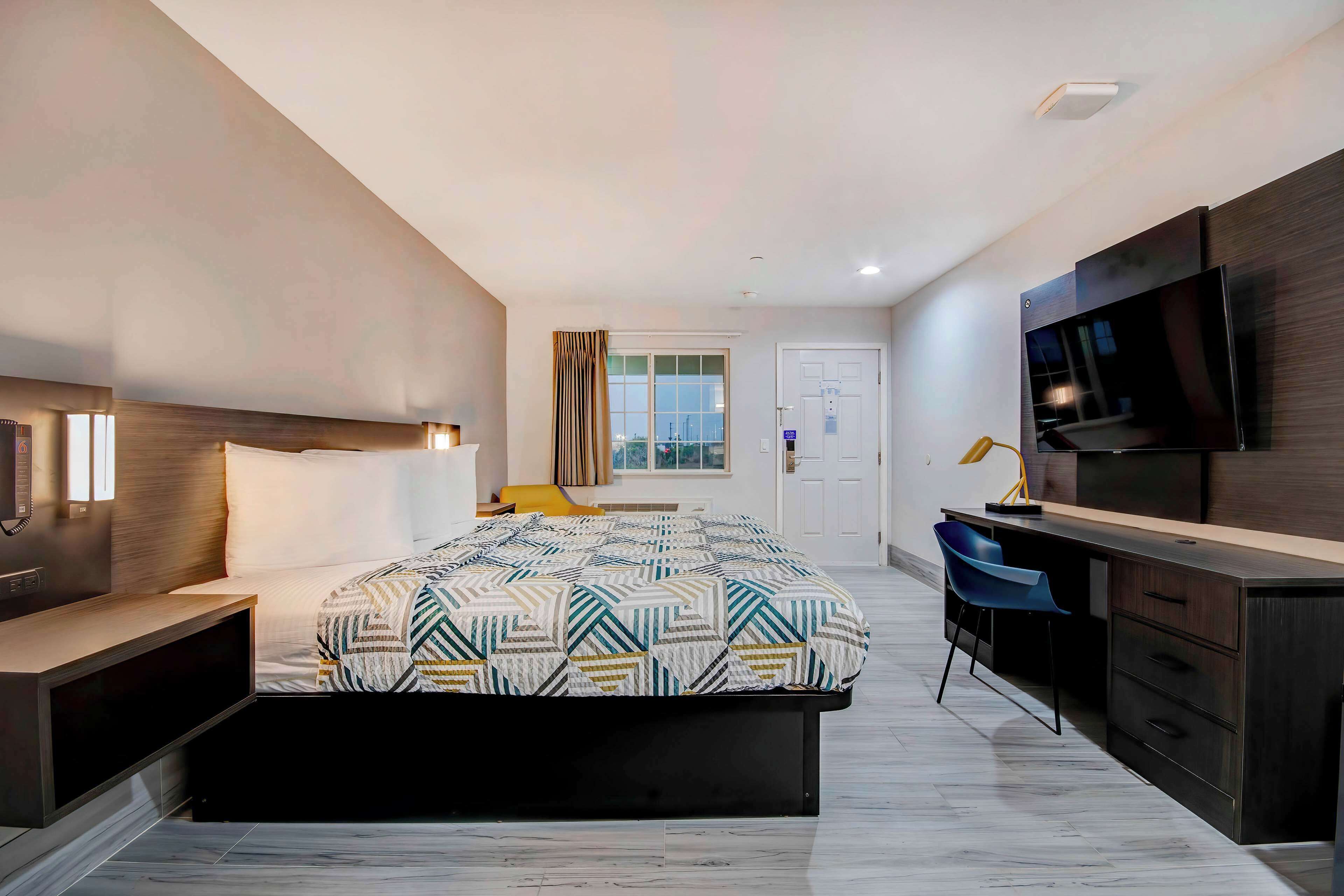 A modern bedroom with a large bed, a desk, and a TV.