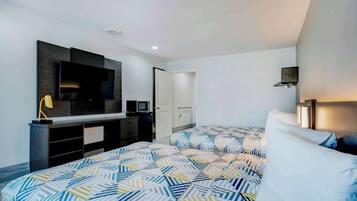 A modern hotel room with a large bed, a flat-screen TV, a desk with a computer, and a door leading to another room.