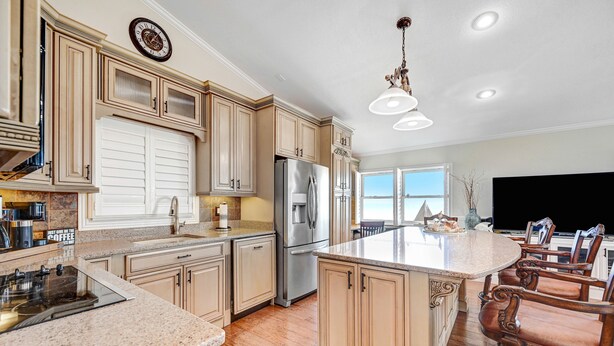 A spacious kitchen with wooden cabinets, a stainless steel refrigerator, and a large island with bar stools. - Spectacular direct ocean front condo with amazing views of the Atlantic (Satellite Beach)