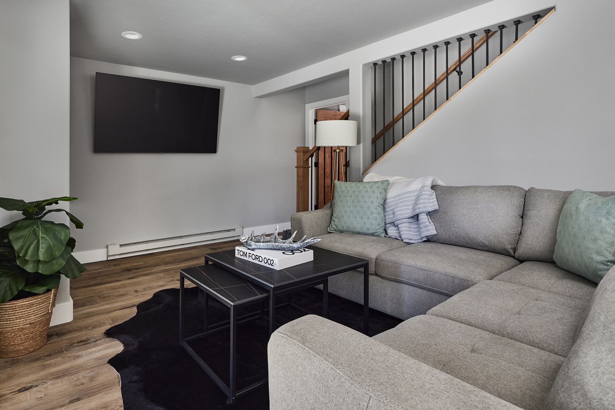 A modern living room with a grey sofa, a black coffee table, and a flat-screen TV mounted on the wall.