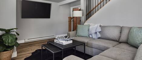A modern living room with a grey sofa, a black coffee table, and a flat-screen TV mounted on the wall.