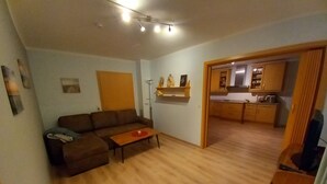 Una sala de estar con sofá, una mesa de centro y una cocina visible a través de un vano abierto.