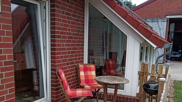 Un patio con un muro de ladrillo, un ventanal corredera y una pequeña mesa con sillas.