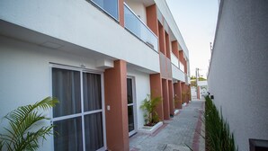 Un edificio moderno con fachada limpia, amplios ventanales y un estrecho sendero con plantas en macetas.