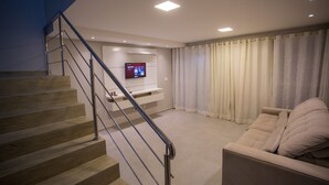 Una sala de estar moderna con una escalera, un televisor de pantalla plana en la pared y un sofá color beige.
