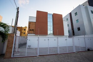 Una entrada protegida con un portón de metal, un muro de ladrillo y un edificio con fachada de vidrio y paneles marrones.