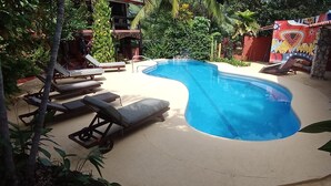 A swimming pool with lounge chairs, surrounded by lush greenery and a colorful mural. - Massai Apartments - Standard Suite (Playa Flamingo)