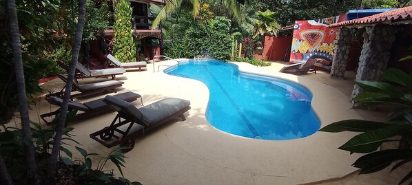 A swimming pool with lounge chairs, surrounded by lush greenery and a colorful mural.