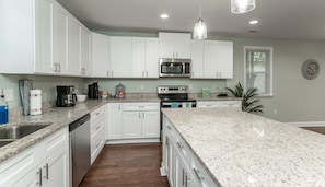 A modern kitchen with white cabinets, stainless steel appliances, granite countertops, and a large island.