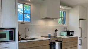 A modern kitchen with white cabinetry, a built-in microwave, a stainless steel sink, a toaster, and a refrigerator.