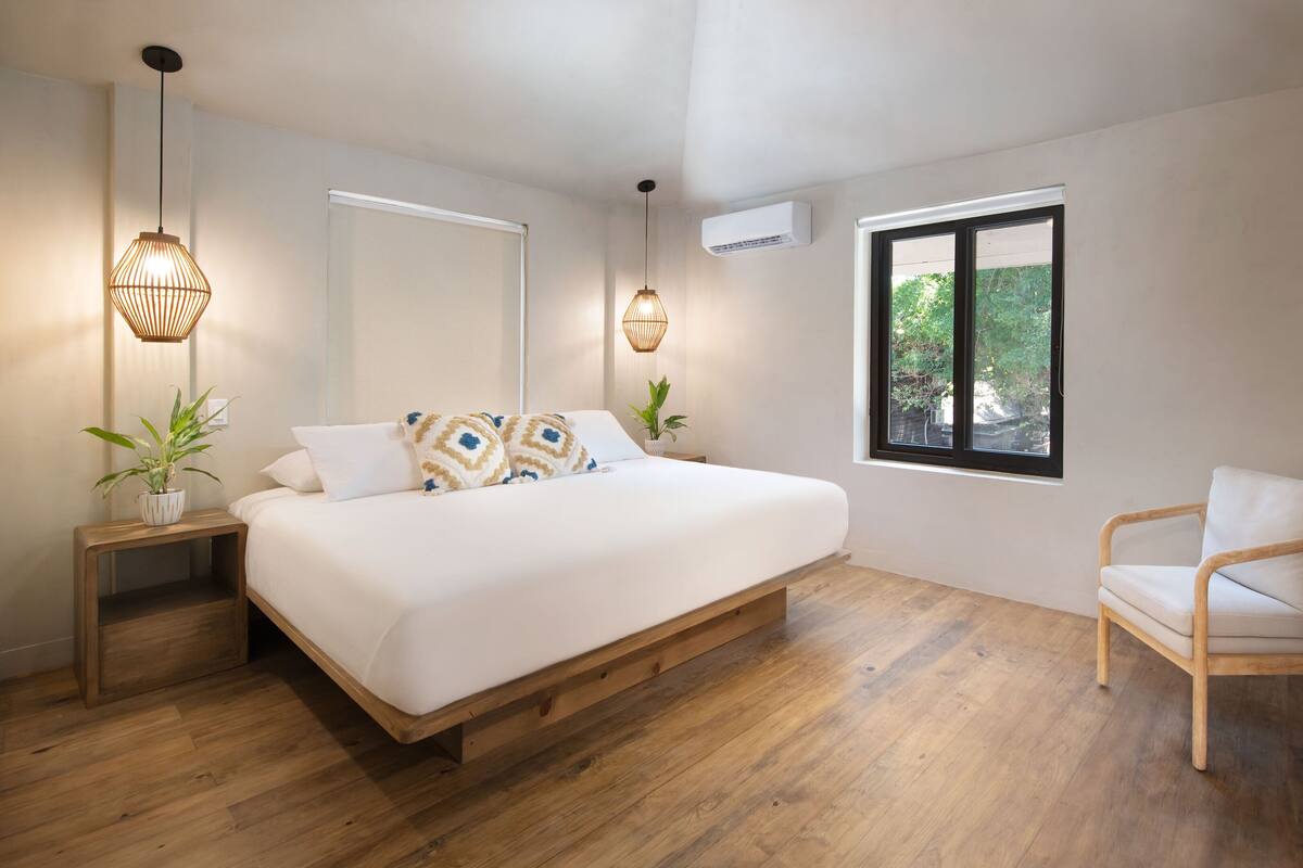 A bedroom with a wooden bed, bedside tables with lamps, a window with a view, and a chair.