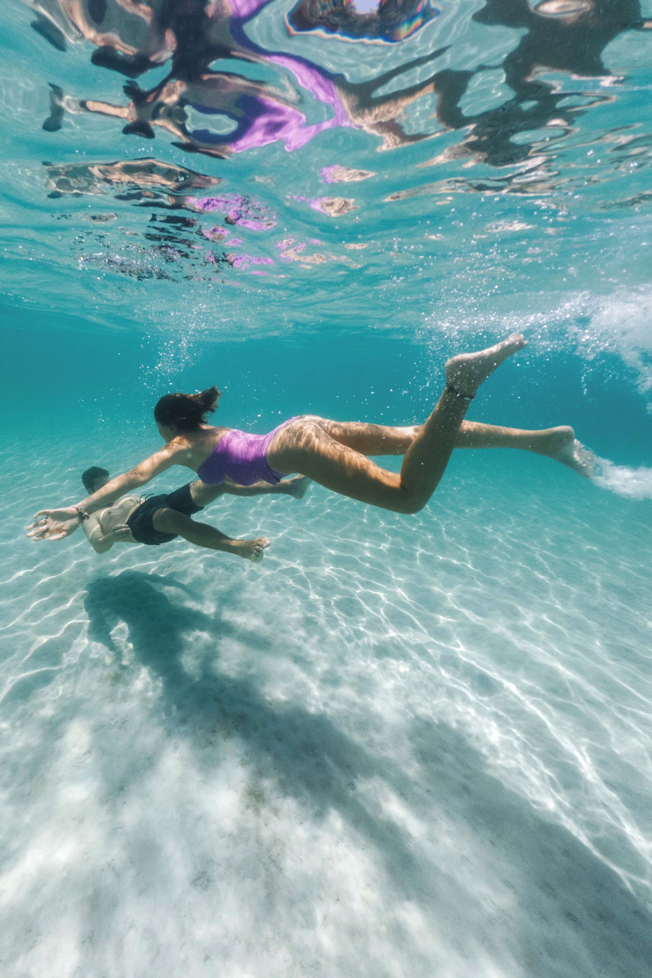 A person swimming underwater in clear blue water.