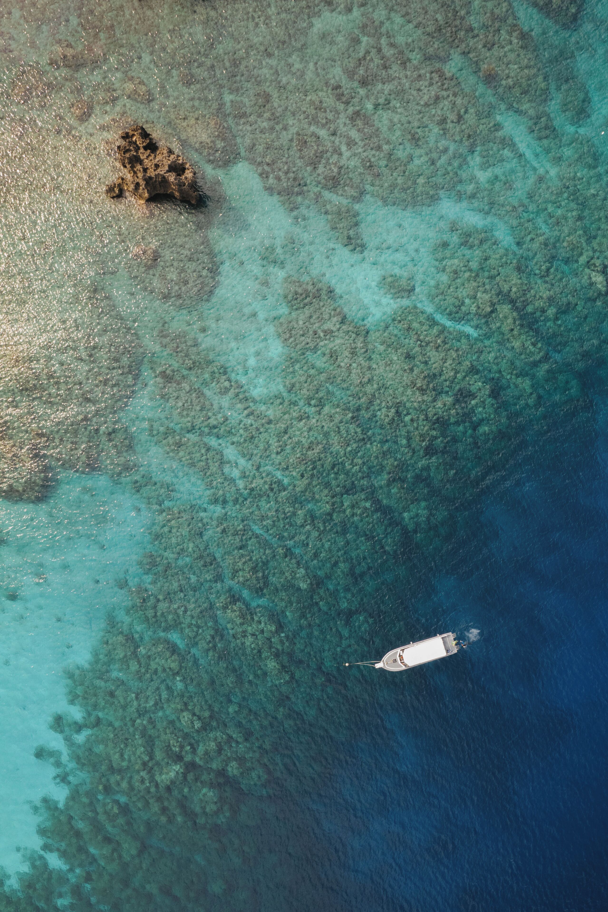 An aerial view of a coastal area with clear turquoise waters, a rocky outcrop, and a boat.